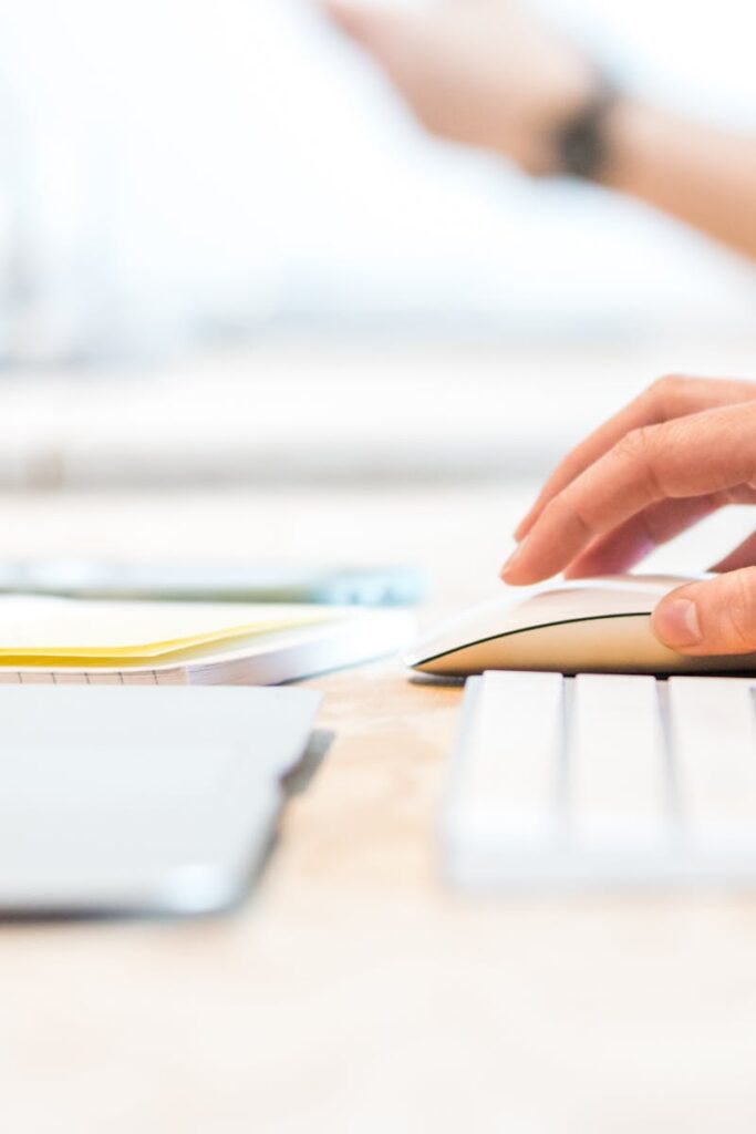 A person working at a laptop with a wireless mouse and keyboard in a bright office setting.